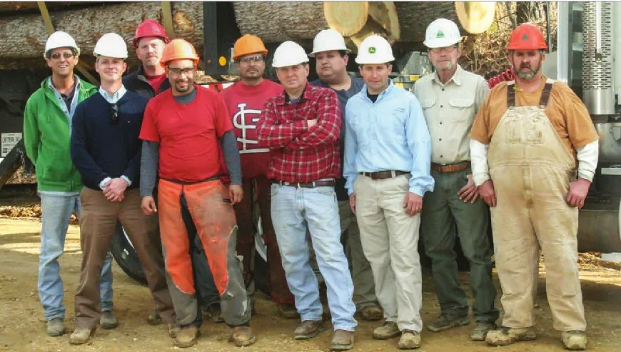 Eleven members of the Wade Norris Logging crew in hard hats standing in front of a loaded log truck